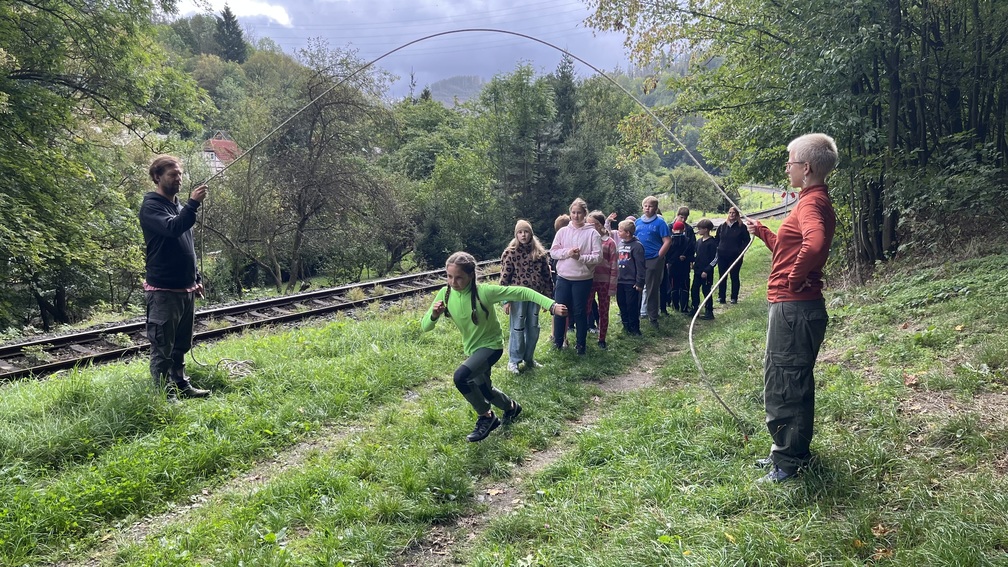 Kinder spielen mit zwei Erwachsenen an einer Bahnstrecke im gruenen Wald