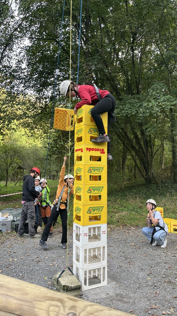 Person mit Helm klettert konzentriert auf hohem Turm aus gelben Kisten