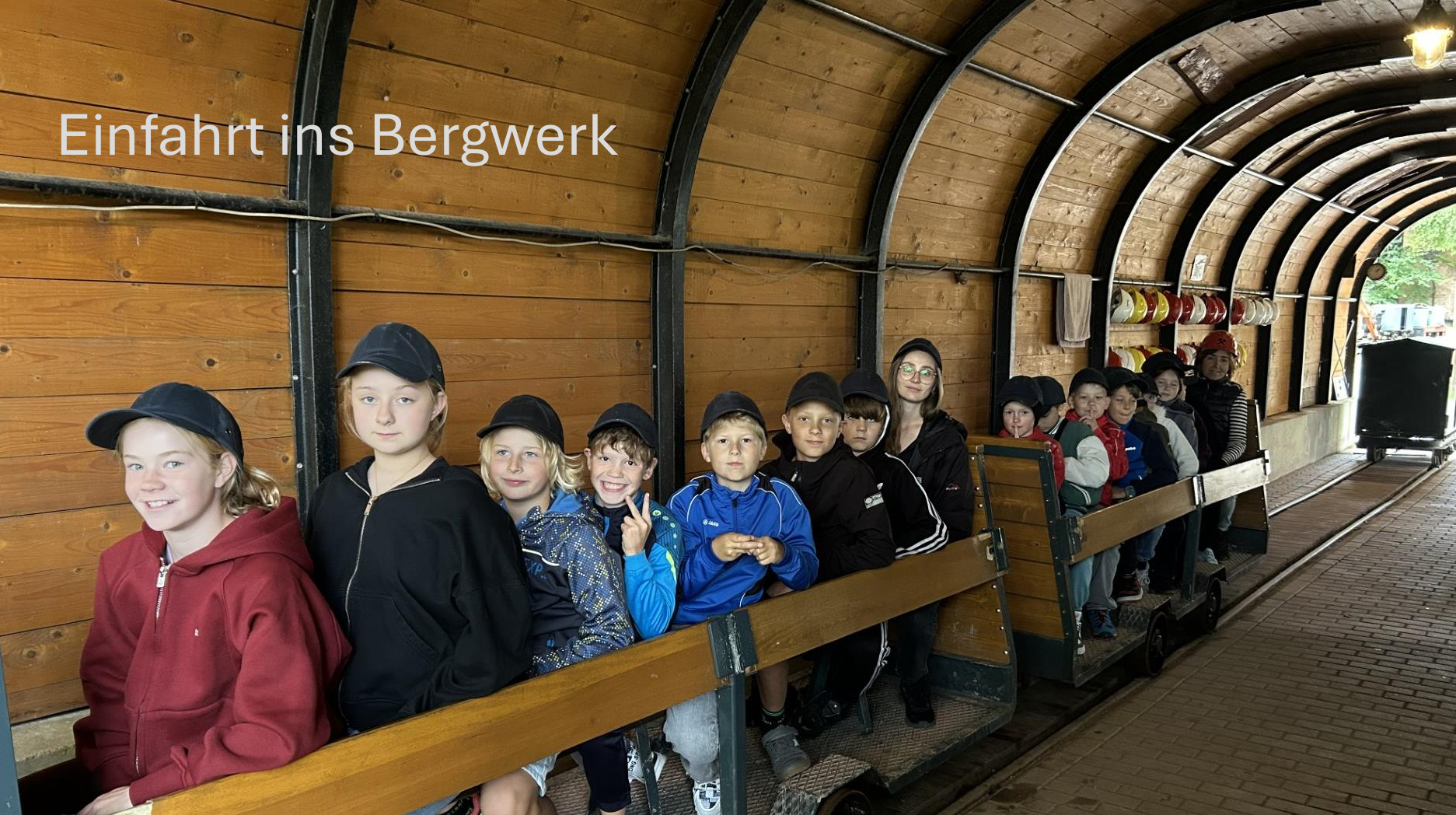 Laechelnde Kinder mit Kappen sitzen in einer Grubenbahn im Bergwerk