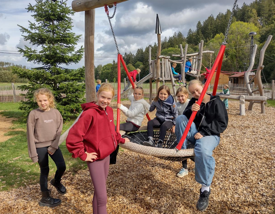 Laechelnde Kinder auf einer Nestschaukel mit roten Seilen am Spielplatz