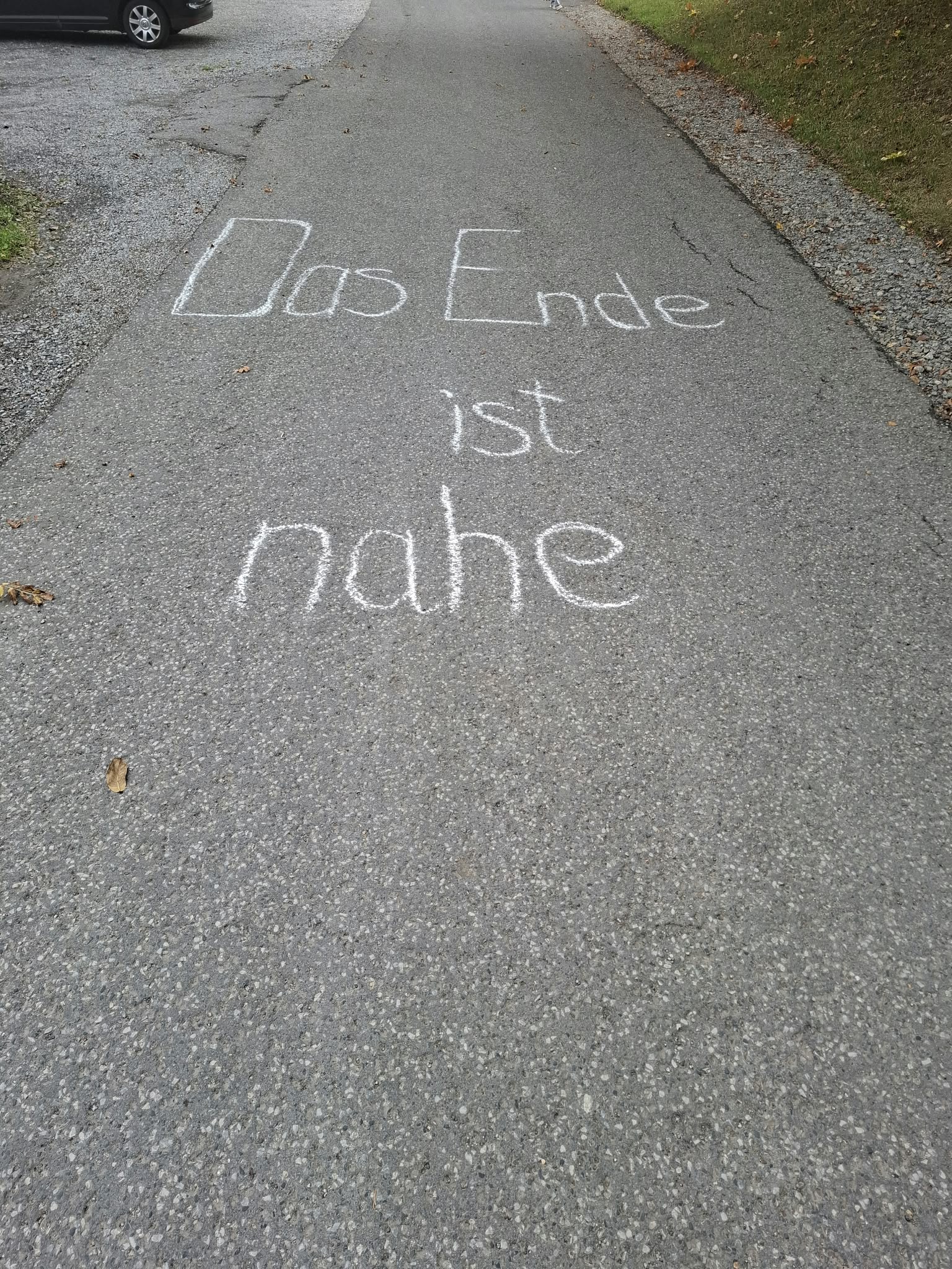 Weisse Kreideschrift Das Ende ist nahe auf grauem Asphaltweg mit Laub